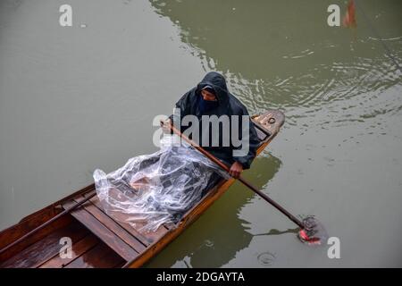 Srinagar, Inde. 08 décembre 2020. Un boatman se couvre de polyéthylène pendant une pluie.des endroits plus élevés de la vallée du Cachemire ont reçu des chutes de neige pour le deuxième jour, tandis que les plaines ont été heurtées par des pluies, a déclaré un responsable. Crédit : SOPA Images Limited/Alamy Live News Banque D'Images