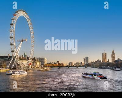 Staycation le London Eye illuminé par le soleil couchant, sur la Tamise avec la Tamise Clipper Boat RB 1 en amont vers London Eye amarré avec le Parlement derrière Londres UK Banque D'Images