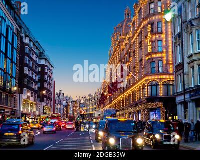 BROMPTON ROAD SUNSET ULEZ HARRODS SOLDE KNIGHTSBRIDGE VENTES TAXIS Brompton Road ventes d'hiver occupé crépuscule boutiques de coucher du soleil y compris Harrods magasin au crépuscule avec le panneau « Sale » éclairé acheteurs les bus rouges et les taxis noirs Knightsbridge Londres SW1 Banque D'Images