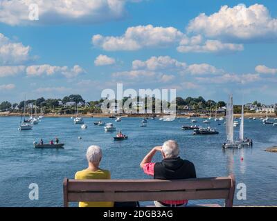 MORBIHAN VACANCES COUPLE VOILE Sentier de la Plage, vieux français détente couple plein air sous le soleil assis regardant diverses activités de navigation voile Golfe du Morbihan, Larmor-Baden, Morbihan, Bretagne, France Banque D'Images