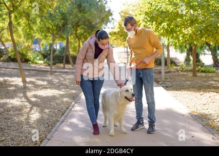 Jeune couple blanc dans des masques chirurgicaux médicaux tenant des promenades avec le chien dans la forêt d'été. Famille, europe, hugs, coronavirus, maladie, infection Banque D'Images