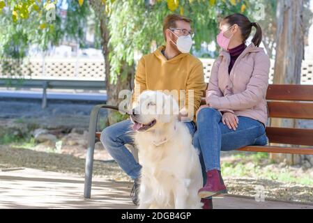 Jeune couple blanc dans des masques chirurgicaux médicaux tenant des promenades avec le chien dans la forêt d'été. Famille, europe, hugs, coronavirus, maladie, infection Banque D'Images