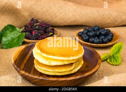 Pile de crêpes dans un bol en bois avec mûre et myrtille en plaque de bois Banque D'Images