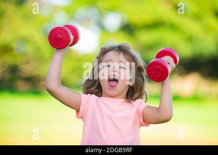 Sport amusant pour enfants. Enfant avec haltères dans le parc. Petit garçon fort. Visage d'enfant amusant. Visages amusants pour les enfants. Enfant drôle avec des haltères. Concept de santé des enfants Banque D'Images