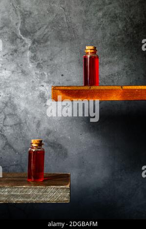 Deux flacons de bouchon en verre contenant du liquide rouge translucide sur du bois etagères sur fond texturé gris Banque D'Images