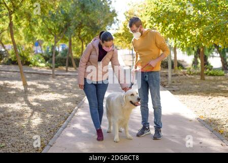 Jeune couple blanc dans des masques chirurgicaux médicaux tenant des promenades avec le chien dans la forêt d'été. Famille, europe, hugs, coronavirus, maladie, infection Banque D'Images