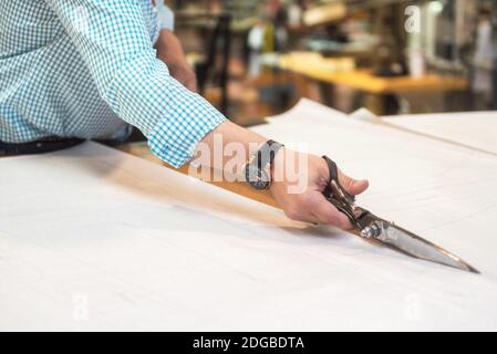 Tailler le motif marqué sur le tissu avec de grandes ciseaux sur l'établi dans son atelier, vue rapprochée de ses mains. Banque D'Images