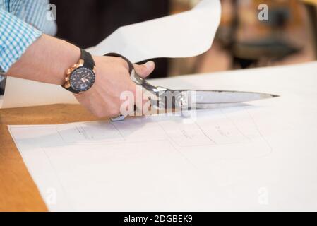 Tailler le motif marqué sur le tissu avec de grandes ciseaux sur l'établi dans son atelier, vue rapprochée de ses mains. Banque D'Images