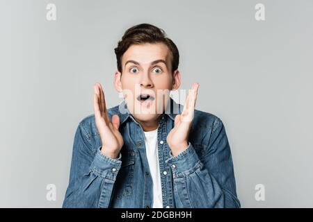 Homme choqué dans une veste en denim regardant la caméra isolée gris Banque D'Images