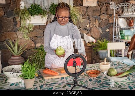 une femme noire avec des lunettes enseigne en ligne avec son téléphone mobile des cours de cuisine à domicile Banque D'Images