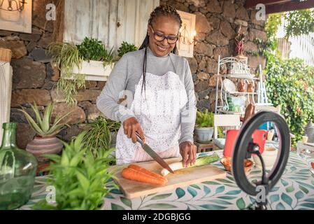 une femme noire avec des lunettes enseigne en ligne avec son téléphone mobile des cours de cuisine à domicile Banque D'Images