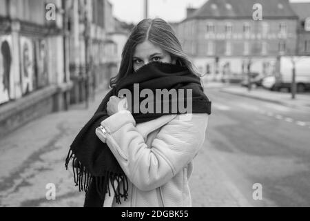 Belle jeune femme adulte portant un foulard noir qui cache le fond de son visage. Elle regarde la caméra. Photographie en noir et blanc. Banque D'Images