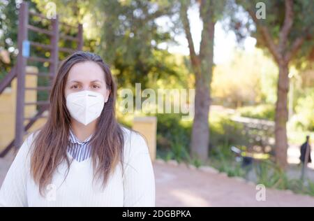 Portrait de heureuse jeune femme portant un masque médical de visage debout par arbre fleuri au printemps Banque D'Images