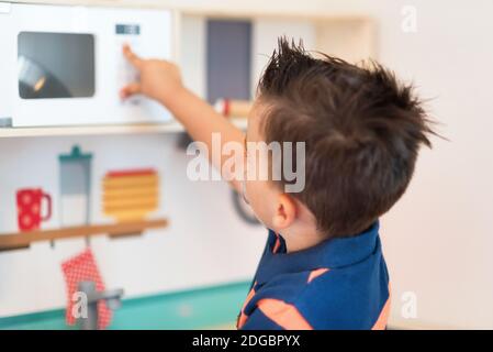 Le petit garçon joue le jeu comme s'il était un cuisinier ou un boulanger dans une cuisine jouet pour enfants. Banque D'Images