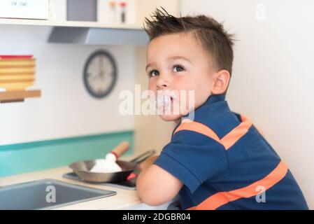 Le petit garçon joue le jeu comme s'il était un cuisinier ou un boulanger dans une cuisine jouet pour enfants. Banque D'Images