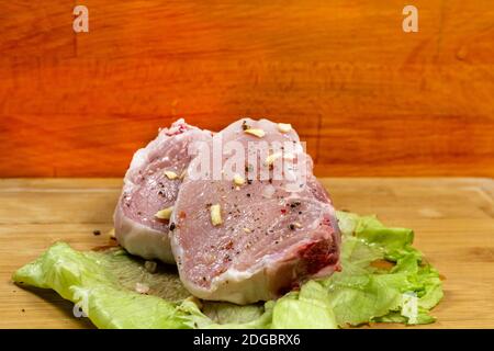 Le steak de porc frais, la viande en tranches crues se trouve sur une feuille de laitue et un fond en bois Banque D'Images