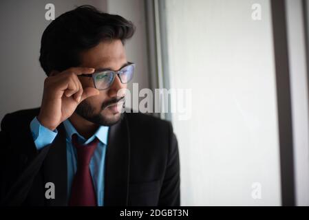 Portrait d'un jeune homme bengali bengali indien haut, sombre et beau en tenue de bureau est debout devant une fenêtre en verre dans un bureau/bpo d'entreprise Banque D'Images