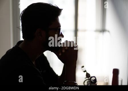 Silhouette d'un bengali indien haut, sombre, belle barbe brune jeune homme en t-shirt décontracté est assis sur une table de bureau dans une humeur créative. Banque D'Images