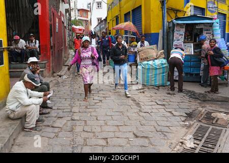 Antananarivo, Madagascar - 24 avril 2019: Deux jeunes filles malgaches inconnues marchant sur une route pavée, plus de gens autour de leurs stands, ou assis o Banque D'Images