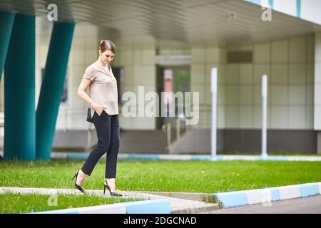 Décontracté jolie jeune femme marchant dans la rue urbaine le jour d'été. Jeans noirs, chaussures à talons hauts. Banque D'Images