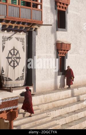 Tôt le matin au monastère d'Hemis. Deux moines se dirigeant vers la salle de prière. Hemis, Ladakh, Jammu-et-Cachemire, Inde. Sur l'écran en tissu à l'entrée se trouve le Dharmachakra - une roue de Dharma typique avec huit rayons - représentant le chemin d'Eightfold - le plus ancien symbole universel pour le bouddhisme. Banque D'Images