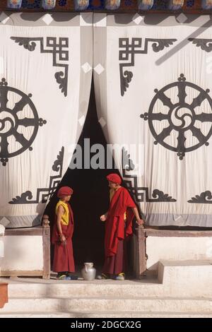 Tôt le matin au monastère de Hemis. Deux jeunes moines à l'entrée de la salle de prière. Sur l'écran en tissu à l'entrée ci-dessus est le Dharmachakra - Banque D'Images