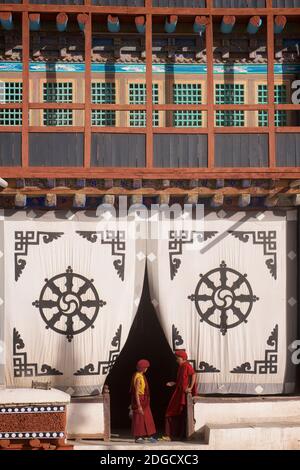 Tôt le matin au monastère de Hemis. Deux jeunes moines à l'entrée de la salle de prière. Sur l'écran en tissu à l'entrée ci-dessus est le Dharmachakra - Banque D'Images