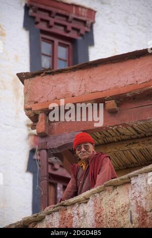 Portrait d'un moine de Ladakhi âgé en peignoirs monastiques, lunettes de soleil et chapeau en tissu rouge. Monastère de Lamayuru, Lamayouro, Ladakh, Jammu-et-Cachemire, Inde Banque D'Images
