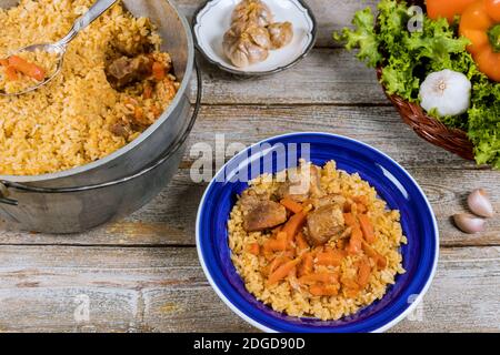 Repas ouzbek traditionnel appelé riz pilaf avec viande, carotte et oignon dans une assiette sur fond de bois vintage Banque D'Images