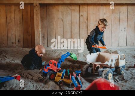 Enfants jouant avec des camions et des creuseurs dans un bac à sable extérieur hiver Banque D'Images