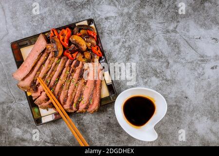 Bœuf rôti de bœuf coréen fait de la sirloin mince de steak frit dans les poivrons rouges et les champignons sur l'assiette avec des baguettes Banque D'Images