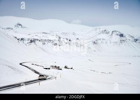 Paysage islandais de montagnes enneigées et route sinueuse avec conduite auto en hiver Banque D'Images