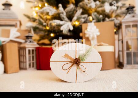 Boîte cadeau ovale écologique décorée de cône et de branche de sapin, arbre de Noël avec cadeaux sur fond flou, emballage réutilisable, foc sélectif Banque D'Images