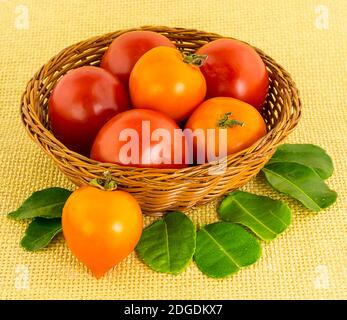 Grande tomate rouge dans un panier brun osier avec un fruits en forme de cœur avec feuilles vertes en gros plan Banque D'Images