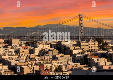 Maisons à flanc de colline de San Francisco et le pont de la baie d'Oakland avec ciel de coucher de soleil. Banque D'Images