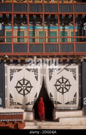 Tôt le matin au monastère de Hemis. Un jeune moine à l'entrée de la salle de prière. Sur l'écran en tissu à l'entrée ci-dessus est le Dharmachakra - une roue typique de Dharma avec 8 rayons représentant le chemin d'Eightfold - le plus ancien symbole universel pour le bouddhisme. Monastère de Hemis, Hemis, Ladakh, Jammu-et-Cachemire, Inde. Banque D'Images