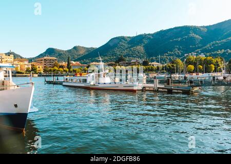 Lac de Côme dans la ville de Côme pittoresque vue panoramique sur l'eau bleue avec yachts blancs et bateaux, montagnes et belle rive de la ville avec des arbres verts sur le Summe Banque D'Images