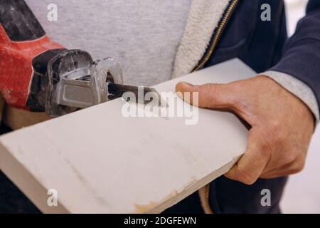 Un homme découpe une planche de bois avec un détail de scie sauteuse d'une planche de bois de coupe avec de la poussière de scie. Banque D'Images