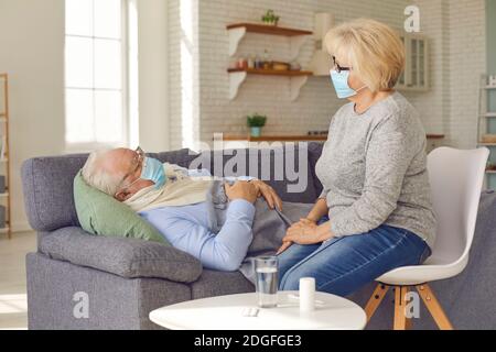 Femme âgée dans un masque de protection médicale prenant soin des personnes âgées le mari ressent de la fièvre Banque D'Images