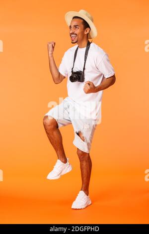Homme de tir vertical sur toute la longueur debout dans le terminal de l'aéroport portant un short, un t-shirt blanc, une pompe de poing triomphante et une empeigne Banque D'Images