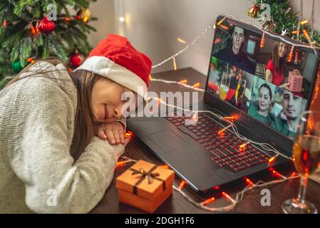 Une jeune femme s'est endormie devant un écran d'ordinateur tout en communiquant avec ses amis et sa famille par liaison vidéo. Concept pour Noël à distance an Banque D'Images