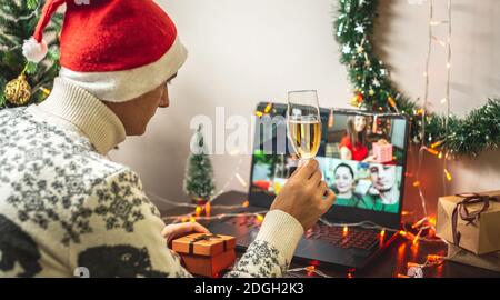Un homme dans un chapeau de père Noël rouge avec une coupe de champagne communique à distance avec ses amis et sa famille via une liaison vidéo. Concept de Noël et du nouvel an Banque D'Images