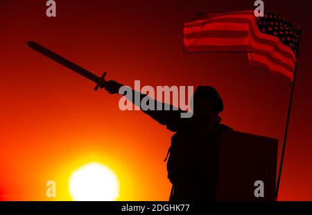 Silhouette d'un soldat de l'armée américaine debout sous le drapeau national, tenant le bouclier, levant et pointant l'épée vers l'avant sur fond de coucher de soleil. Le devoir et l'honneur des soldats, le héros national et le concept de victoire militaire Banque D'Images