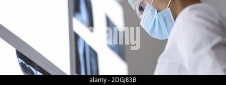Le médecin en masque médical et lunettes de protection regarde une radiographie. Banque D'Images