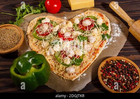 Pizza avant cuisson, légumes et épices sur fond de bois sombre Banque D'Images