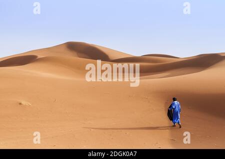 Une personne en vêtements traditionnels marche à travers les dunes de sable au Sahara, au Maroc, en Afrique. Banque D'Images