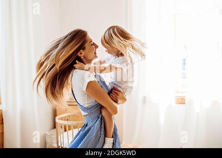 Jeune mère ou baby-sitter avec une petite fille en elle les bras tournent au milieu de la pièce Banque D'Images