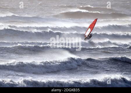 Planche à voile avec voile rouge dans la mer agitée, vagues et vents forts Banque D'Images