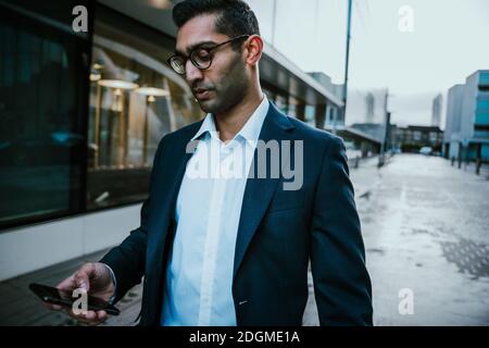 Homme d'affaires de course mixte marchant au travail pour vérifier les dates sur smartphone avant la conférence Banque D'Images