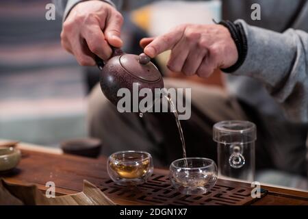 Gros plan avec les mains d'un maître de cérémonie de thé dans un magasin de thé, verser le thé pour la dégustation dans des tasses spéciales sur une table en bambou avec un plateau Banque D'Images